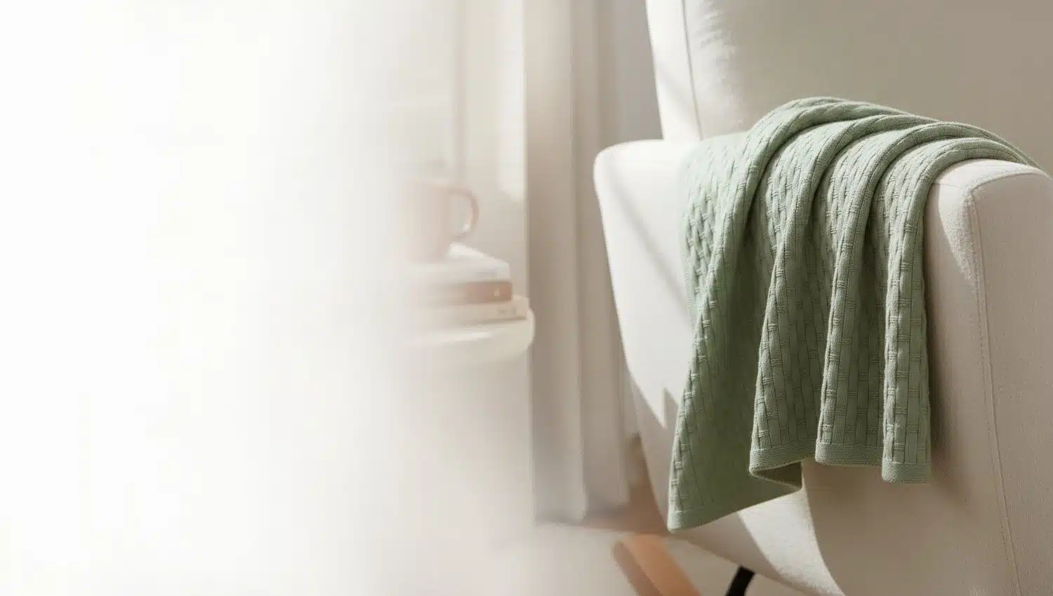 A stocked sage Lattice Blanket draped over a cream armchair